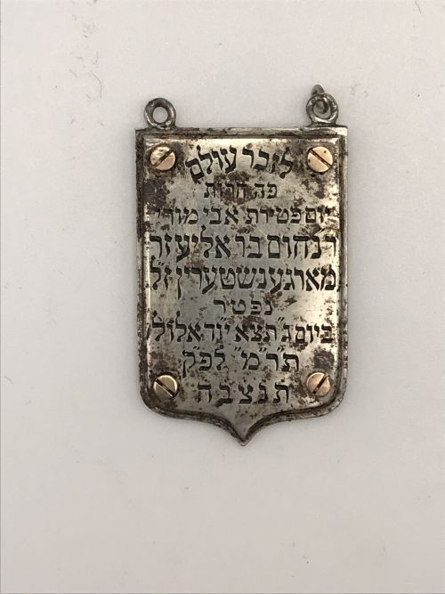 a silver pendant in the shape of a shield with an inscription in Hebrew