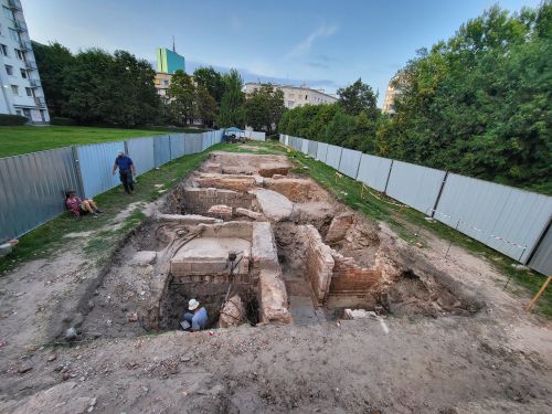 people working in an archaeological trench, with buildings and trees in the background