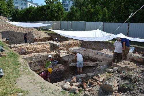 a group of people working in an archaeological trench, sheltered by the sun by awnings