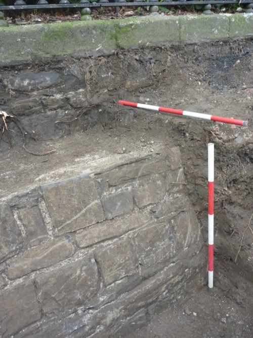 an uncovered wall in an archaeological trench and measuring tools